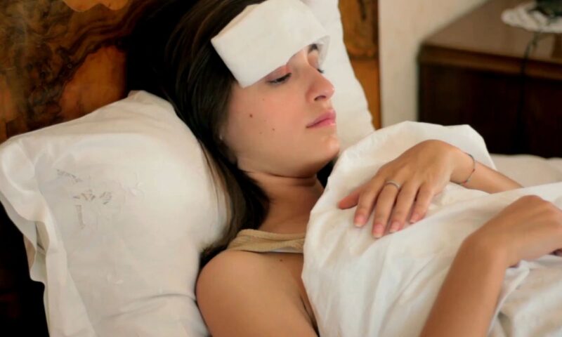 devojka sa temperaturom leži u krevetu sa oblogom na glavi